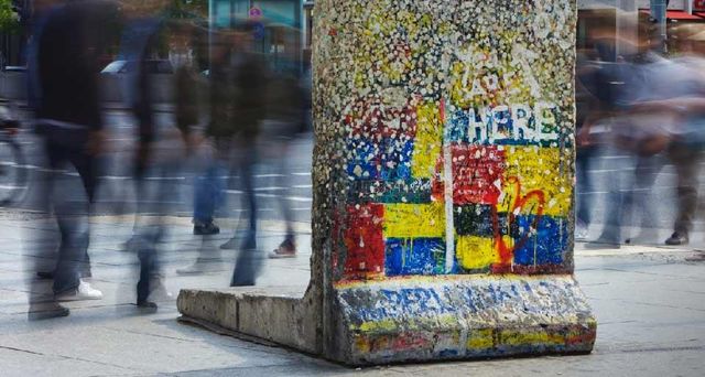 Berliner Mauerdenkmal am Potsdamer Platz. Passanten laufen an einem einzelnen Segment der Berliner Mauer am Potsdamer Platz vorbei, welches an seiner ursprünglichen Position belassen wurde und nun als Denkmal dient.