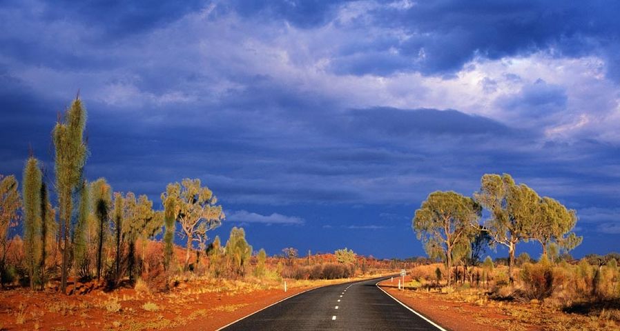 Dark storm clouds gather over Australia's Lasseter Highway as it winds through the red sand desert
