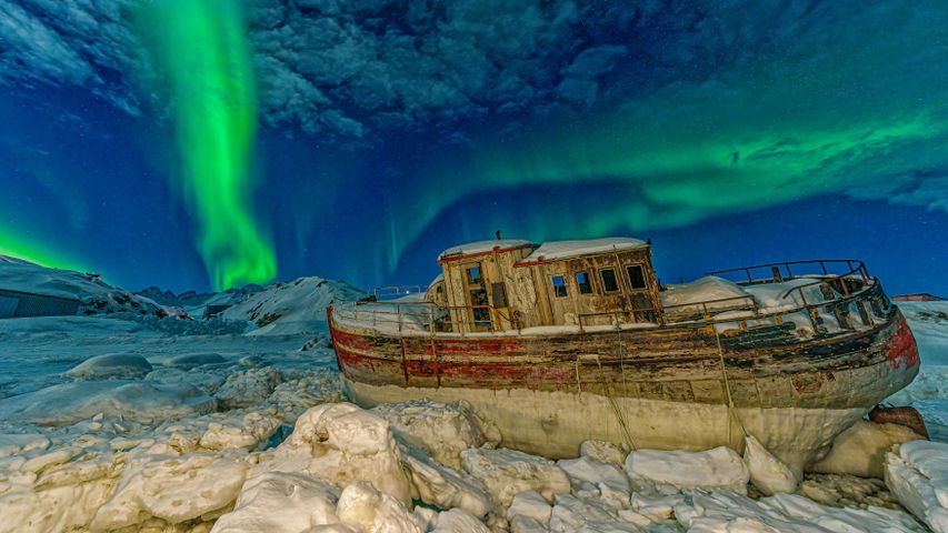 Nordlicht über einem gestrandeten Boot in Tasiilaq, Grönland