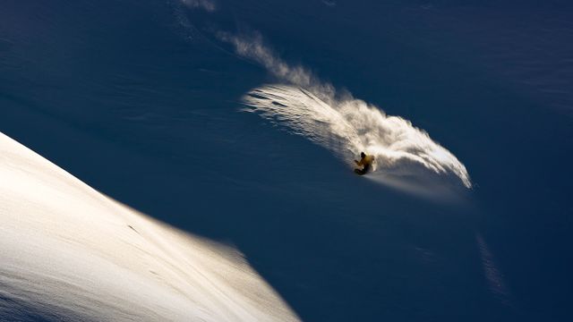 Snowboarder makes powder turn in backcountry terrain