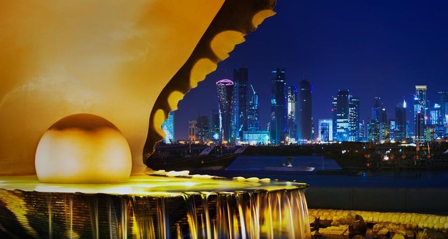 The pearl monument in the Corniche neighbourhood of Doha, Qatar, illuminated at night with the new high-rises of West Bay in the background
