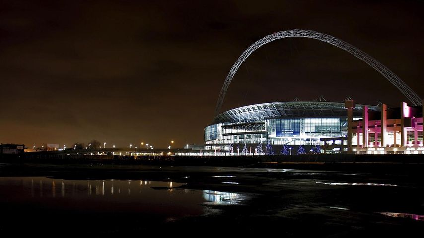 A view across the water to an illuminated Wembley Stadium at night