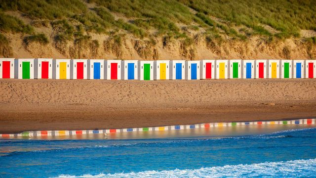 Beach huts reflecting in the water at Woolacombe Beach, Devon 