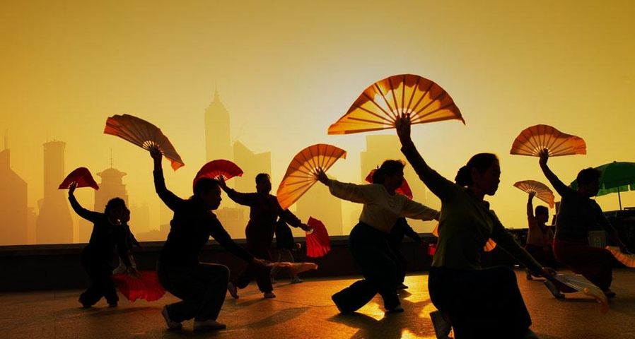 Frauen tanzen mit einem Fächer am Bund, einer Uferpromenade, gegenüber dem Pudong-Distrikt in Shanghai, China