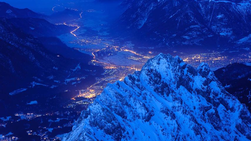 Blick von der Zugspitze auf den Waxensteinkamm und das erleuchtete Garmisch-Partenkirchen, Bayern, Deutschland