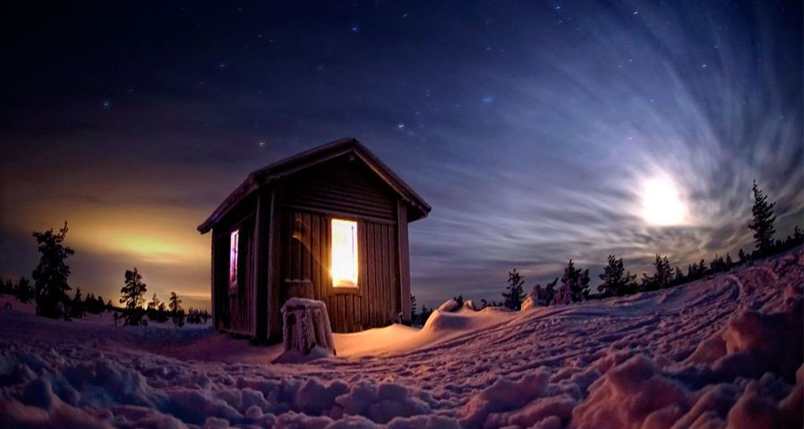 Mountain hut in wilderness with stars and moon at night during winter, Finland