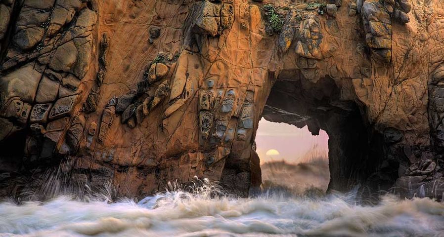 Waves and sea spray through a sea arch at Pfeiffer Beach in Big Sur, California