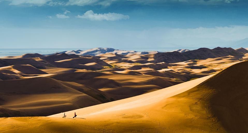 Sandboarders hiking up dunes for another ride, Great Sand Dunes National Park, Colorado, U.S.A.