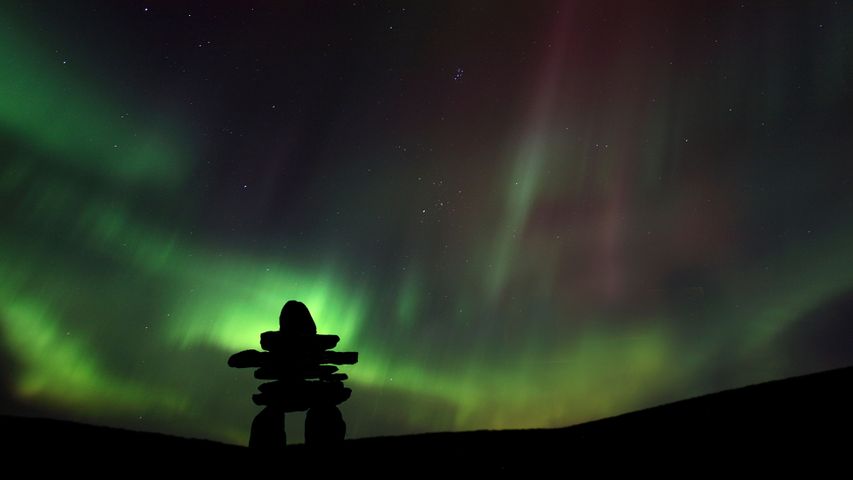 Inukshuk silhouetted against the Northern Lights in Barren Lands, Northwest Territories, Canada