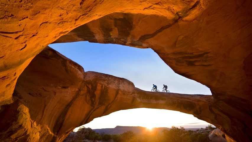 Passeando de Bicicleta em um arco natural de pedra, num deserto próximo à Moab, em Utah, nos Estados Unidos