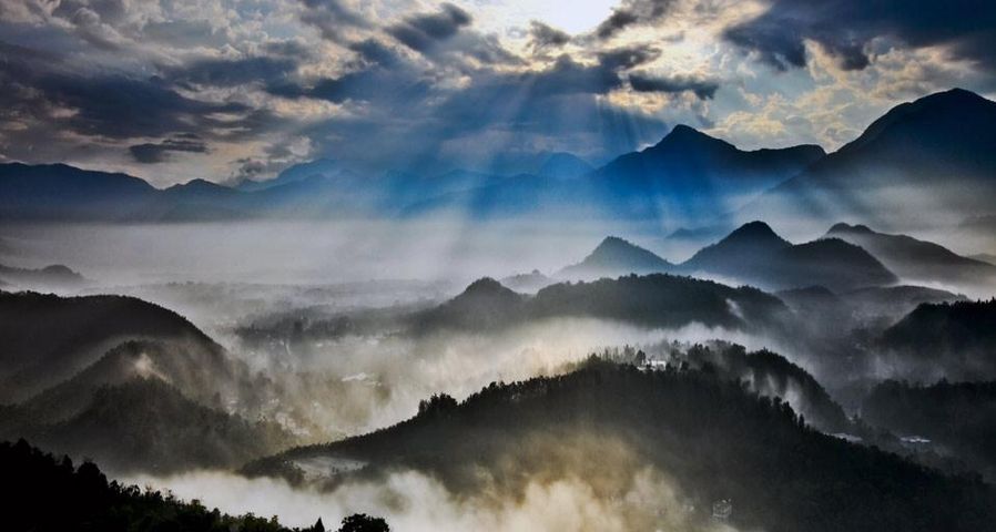 Sun rays slanting into misty valleys below conical peaks in Nantou County, Taiwan