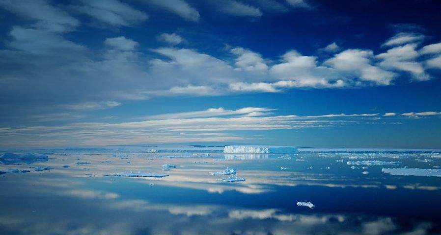 Antarctic iceberg and cloud landscape reflecting in totally calm waters near Ross Island, Antarctica