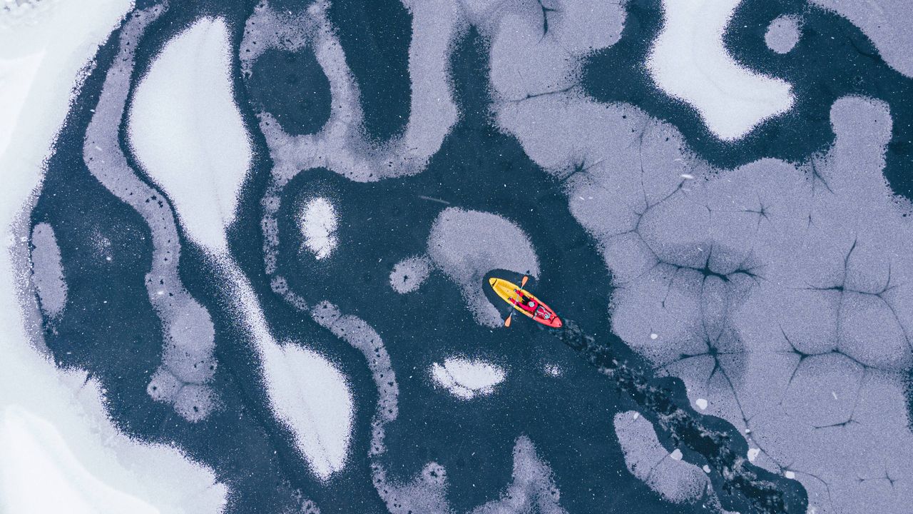 Yellow kayak breaking ice, frozen water patterns