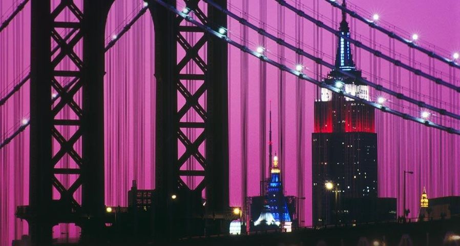 Manhattan Bridge and the Empire State Building illuminated with red, white, and blue lights in New York City, New York