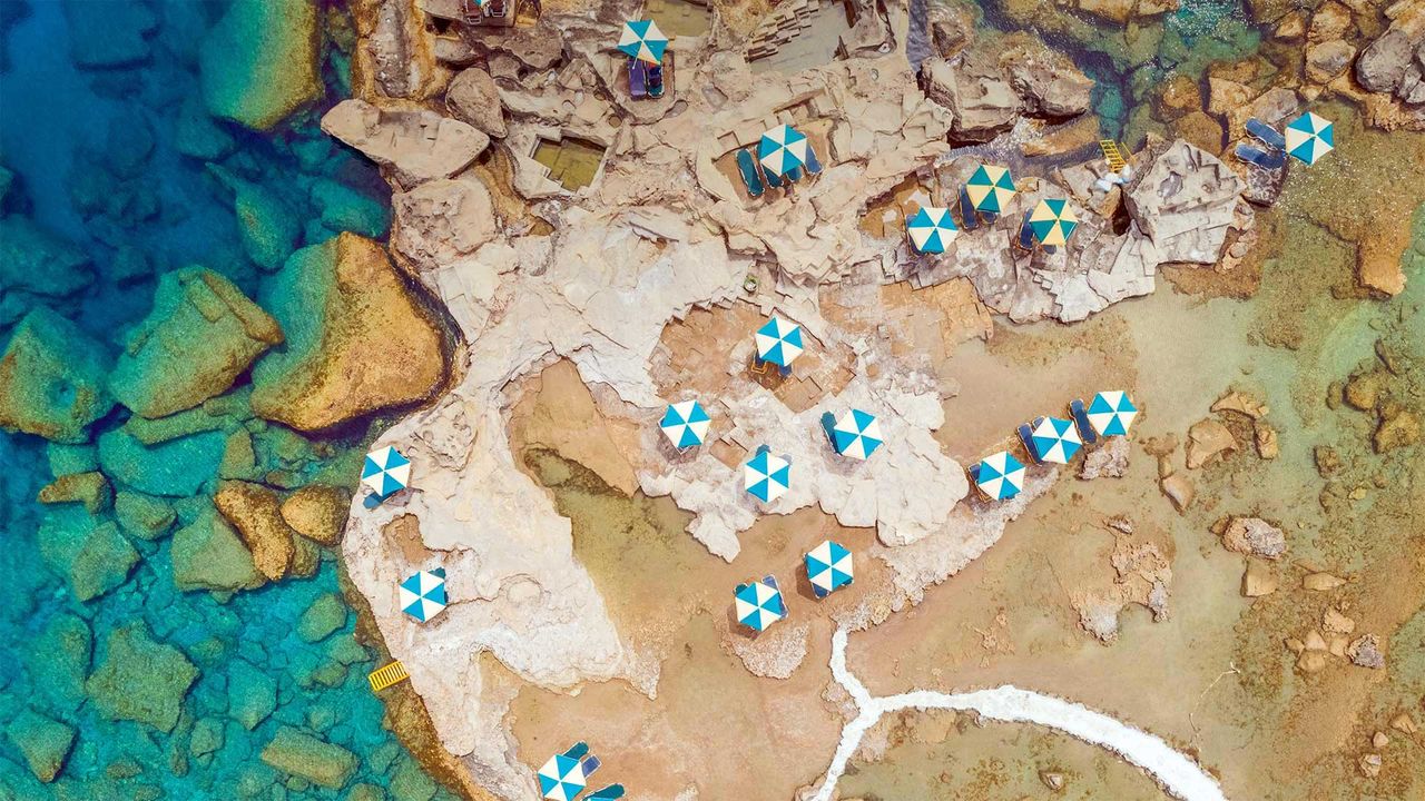 Aerial view of blue and white parasols on the rocky coast of Rhodes, an island in Greece