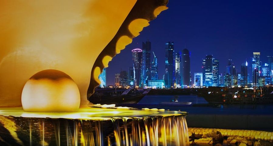 The pearl monument in the Corniche neighborhood of Doha, Qatar, illuminated at night with the new high-rises of West Bay in the background