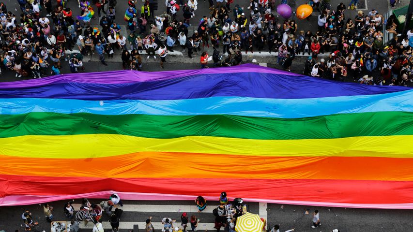 Foliões enchem as ruas segurando uma bandeira gigante do arco-íris durante a parada anual do orgulho LGBT na avenida Paulista