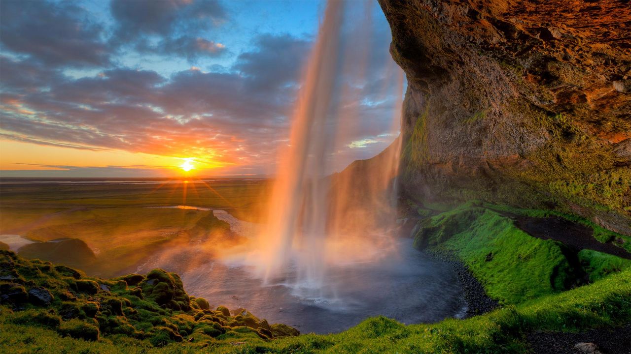 View of the midnight sun behind Seljalandsfoss waterfall near the south coast of Iceland