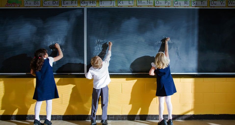 Three students writing on blackboard in classroom