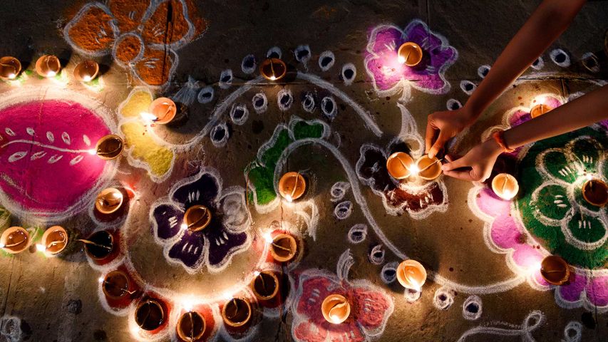 Oil lamps being arranged on rangoli during Diwali