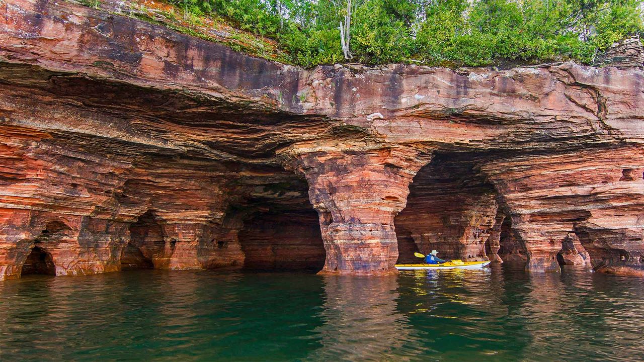Kayaker exploring sandstone sea caves in Apostle Islands National Lakeshore near Bayfield, Wisconsin