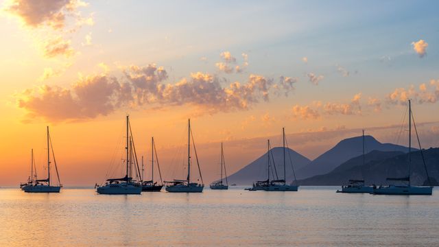 Cielo colorato al tramonto sopra barche a vela ormeggiate, Isole Eolie, Messina, Sicilia, Italia
